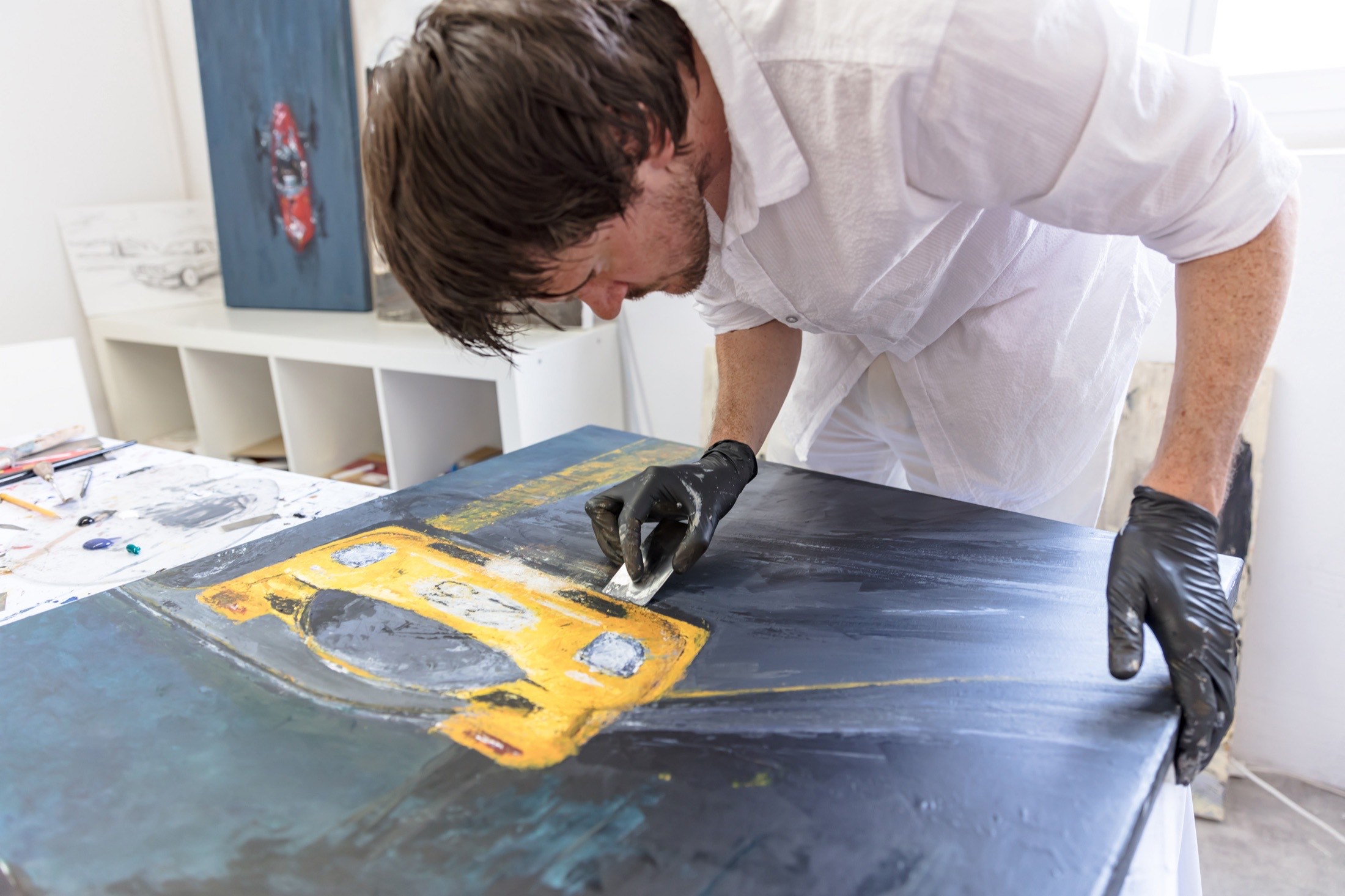 Simon Haener leans over a picture of a yellow racing car
                  with black gloves and a blade